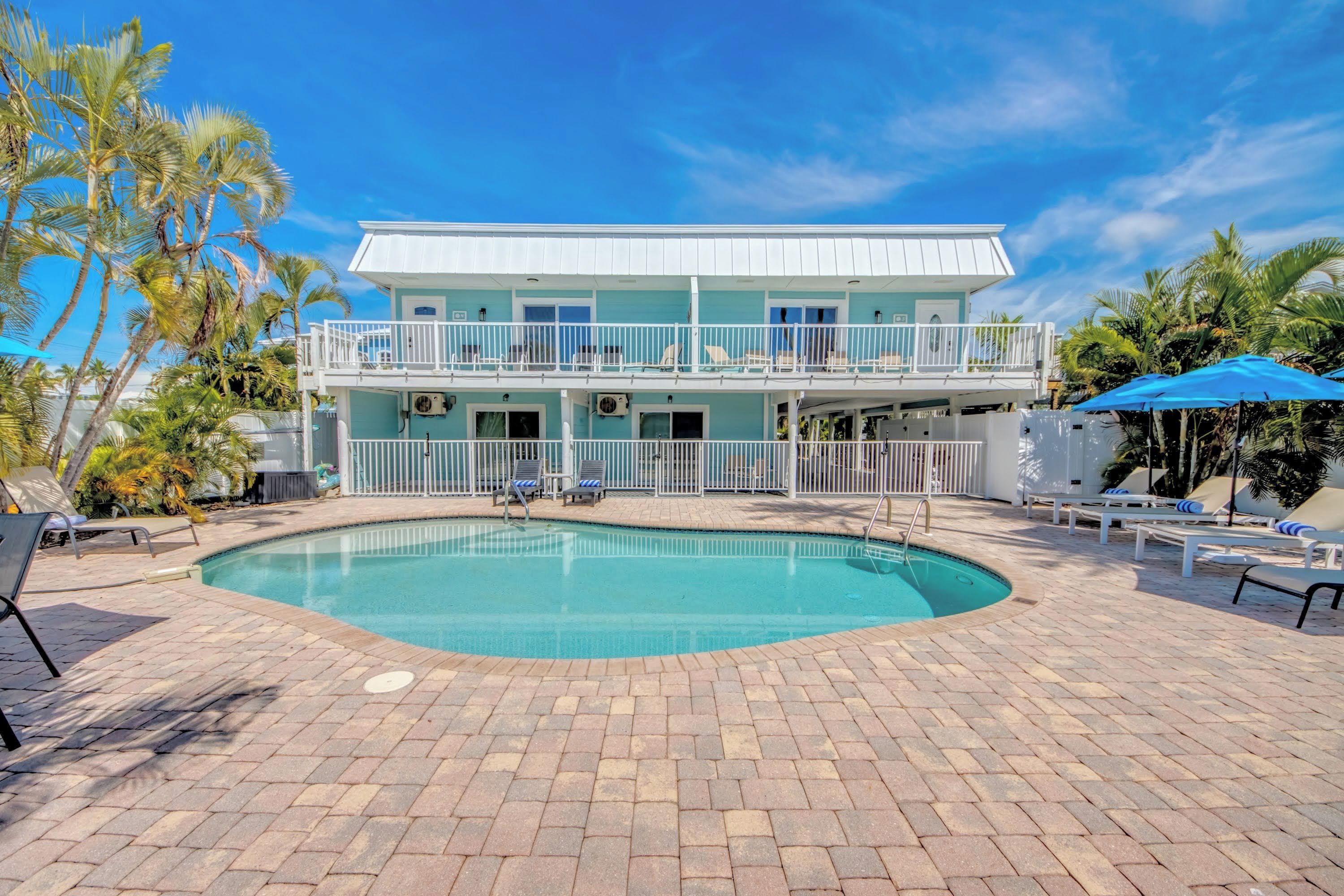 A two-story building with a swimming pool, outdoor seating, and palm trees.