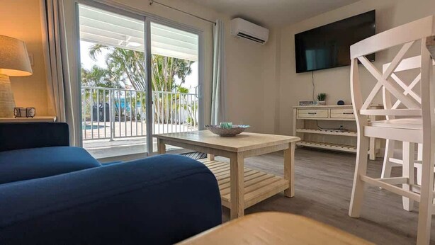 Una habitación con sofá, una mesa con un bol, televisión, una silla y un balcón con barandilla.
