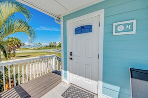 Una casa con fachada azul, una puerta blanca y un balcón con suelo de madera.
