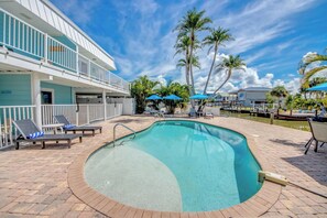 A pool area with lounge chairs, a pool, and a building with balconies.