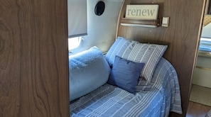 A cozy bed with striped bedding and a pillow, a wooden headboard, and a 'renew' sign on the wall.