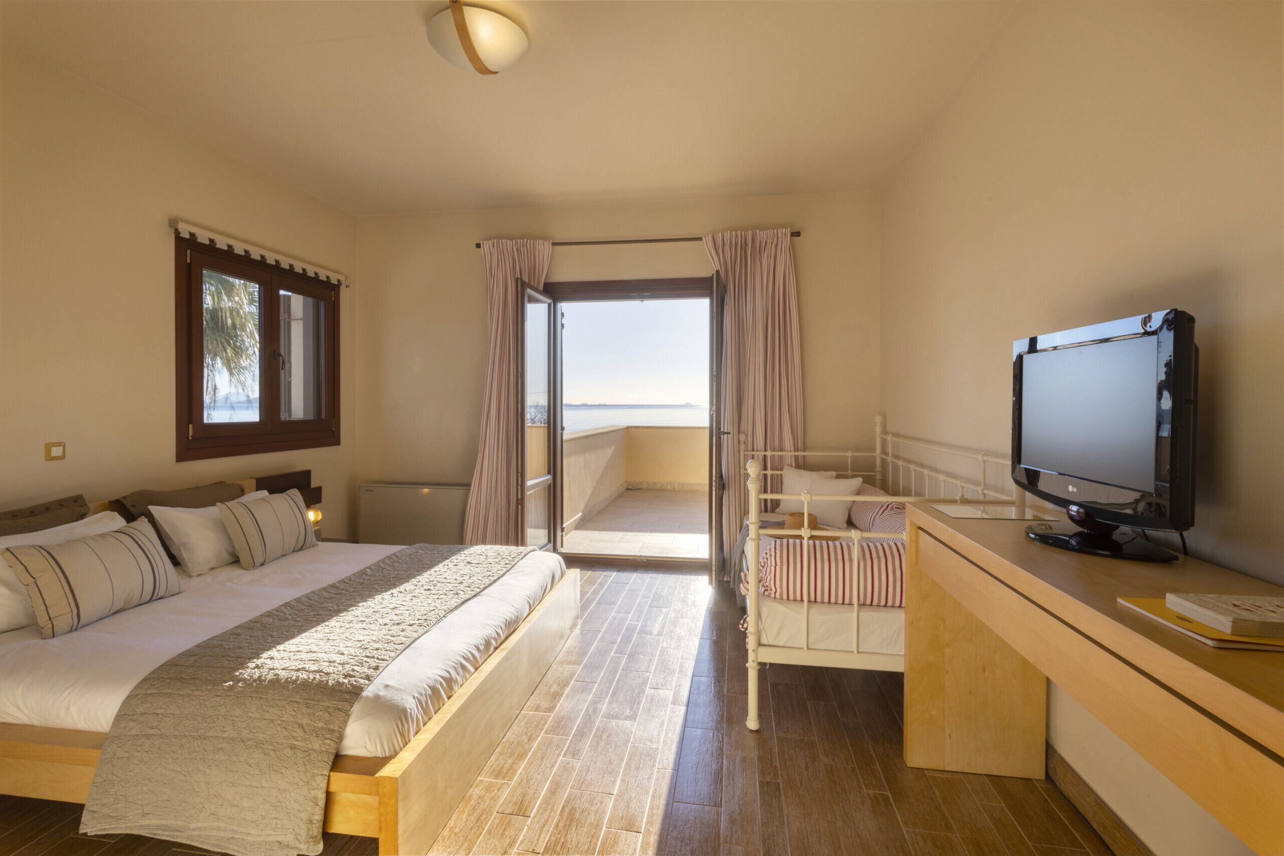Ein Schlafzimmer mit Bett, Schreibtisch und Fernseher, mit Blick aufs Meer durch eine offene Tür.