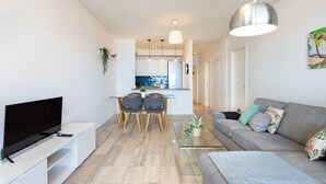 En moderne stue med et fladskærms-tv, en sofa og et sofabord. I baggrunden er der et spiseområde med et bord og stole.