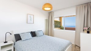 Et soveværelse med seng, natbord, lampe, et vindue med gardiner og udsigt til det fri.
