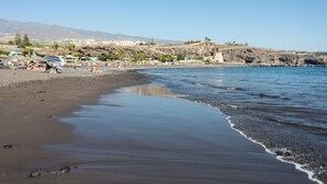Ein Strand mit felsigem Ufer, Sonnenschirmen und Menschen.