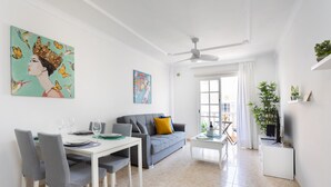 Ein modernes Wohnzimmer mit Essbereich, einem grauen Sofa, einem Deckenventilator und einem großen Fenster mit Vorhängen.
