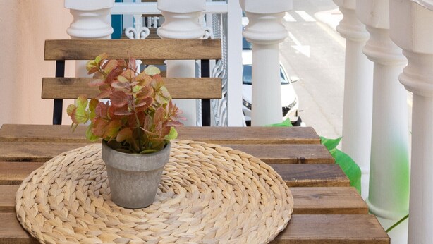 Ein Balkon mit einer gewebten Matte, einer Holzbank und einem Blumentopf.