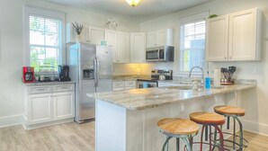 A modern kitchen with white cabinets, stainless steel appliances, a marble island with bar stools, and a window providing natural light. - Family Beach Escape | 3 Pools, Hot Tub & Gulf Beaches Nearby (Port St. Joe)