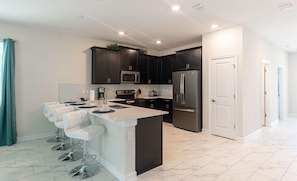 A modern kitchen with dark cabinets, stainless steel appliances, and a central island with bar stools.