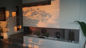 A modern interior with a minimalist design, featuring a white reception desk, a wall-mounted clock, and a small shelf with decorative items.