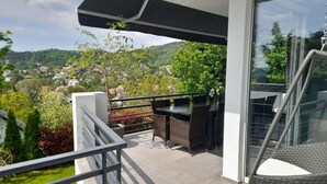 A balcony with a view of a hillside, wicker furniture, and a glass door.