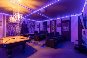 Relax in style with a pool table, reclining chairs, and ambient lighting, surrounded by artwork and a unique chandelier.