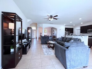 A modern living room with a television, sofa, and coffee table. There is a kitchen area with cabinets and appliances.