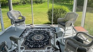En overdækket terrasse med fletstole, et mønstret tæppe og udsigt over et grønt landskab.