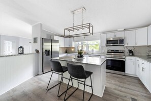 A modern kitchen with white cabinetry, a central island with bar stools, stainless steel appliances, and a pendant light. - Hillside LKN - Lakefront - Priv Dock, Family Fun - Lake Norman Vacation Rental (Mooresville)