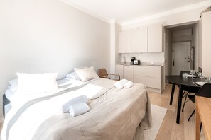 A modern hotel room with a large bed, a small kitchenette, a dining table, and a door leading to a bathroom. - 2ndhomes Modern Studio close to the Sea (Helsinki)