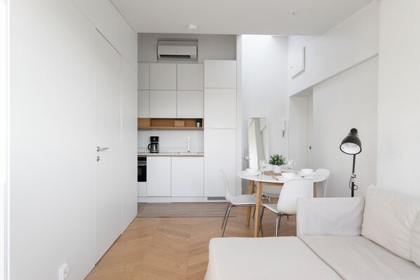A modern, minimalist room with a bed, a dining table with chairs, a kitchen area, and a small plant. - 2ndhomes Modern Studio close to the Sea (Helsinki)