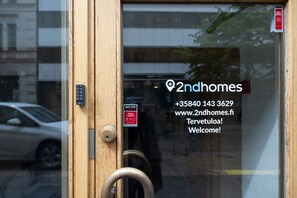 A wooden door with a keypad lock, a sign indicating a sector alarm, and a glass window with a 2ndhomes logo and contact information. - 2ndhomes Modern Studio close to the Sea (Helsinki)