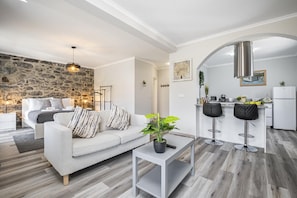A modern living room with a sofa, a coffee table, and a kitchen area with a bar. - Basalt House A by Homie (São Vicente)