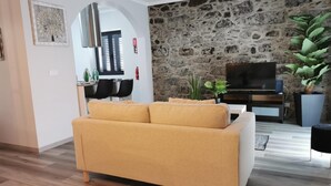 Una sala de estar con sofá, pared de piedra, televisor y planta.
