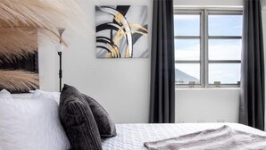 Een moderne slaapkamer met een groot bed, een schilderij aan de muur en een raam met gordijnen.
