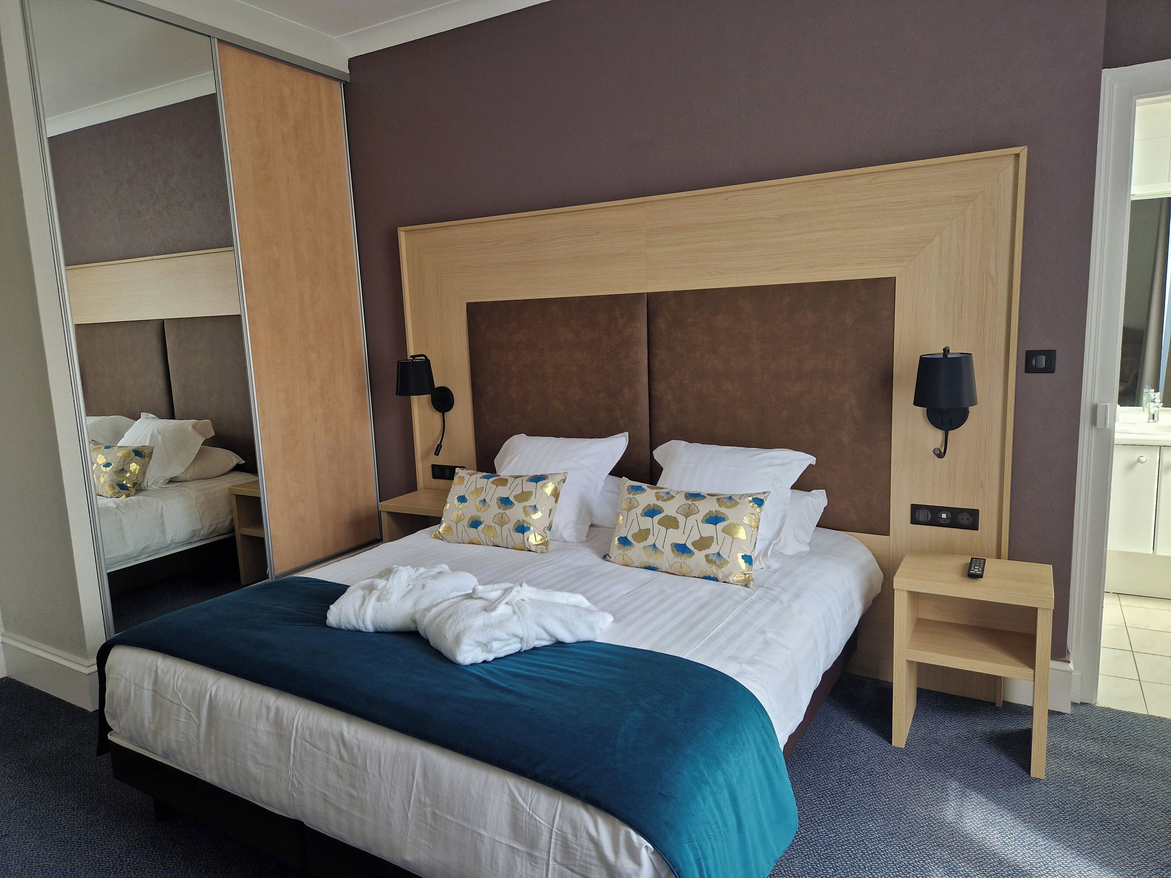 Hotellihuone, jossa on suuri sänky, kaksi yöpöytää, peili ja vaatekaappi.