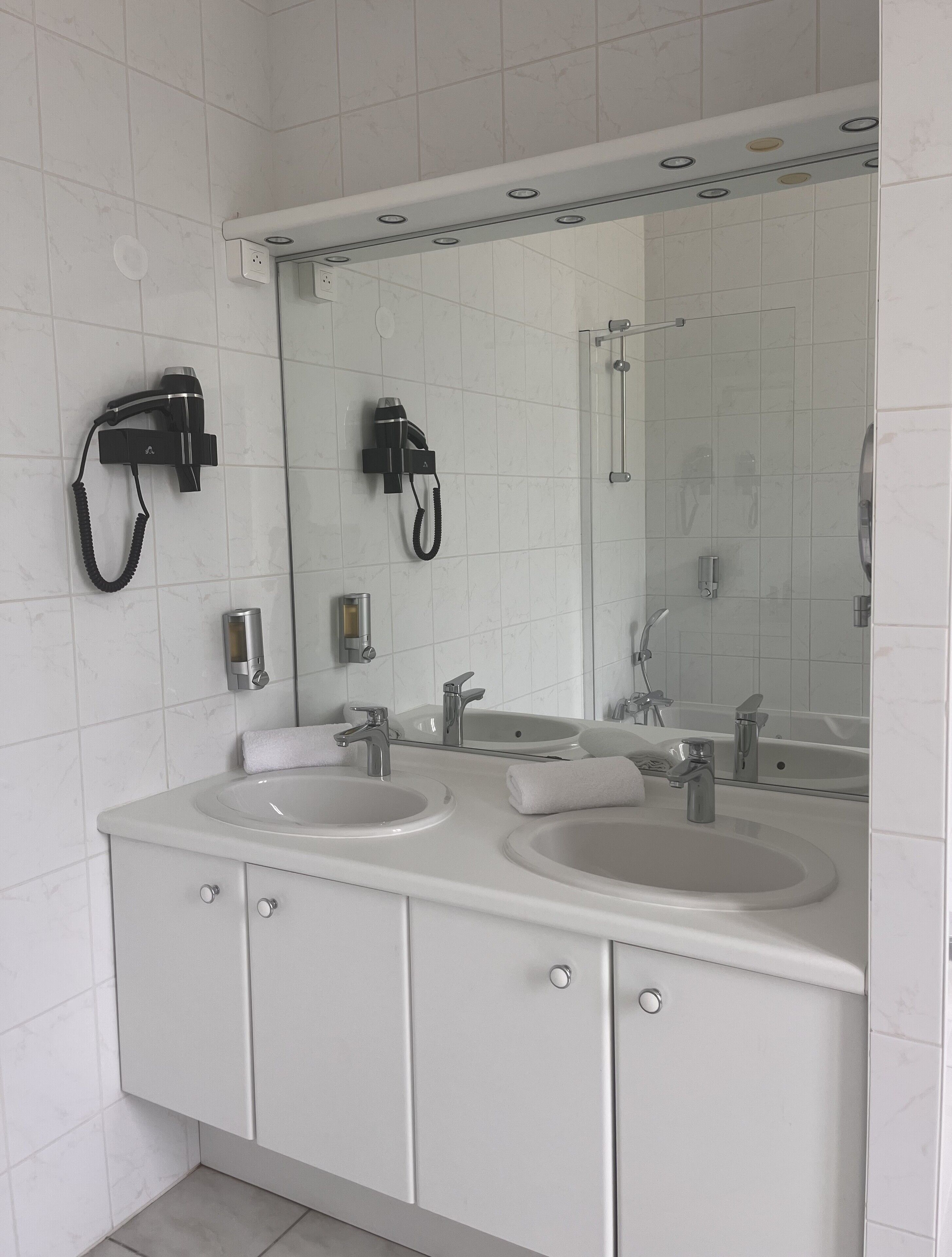 Un baño moderno con dos lavamanos, un espejo grande y un secador de pelo montado en la pared.