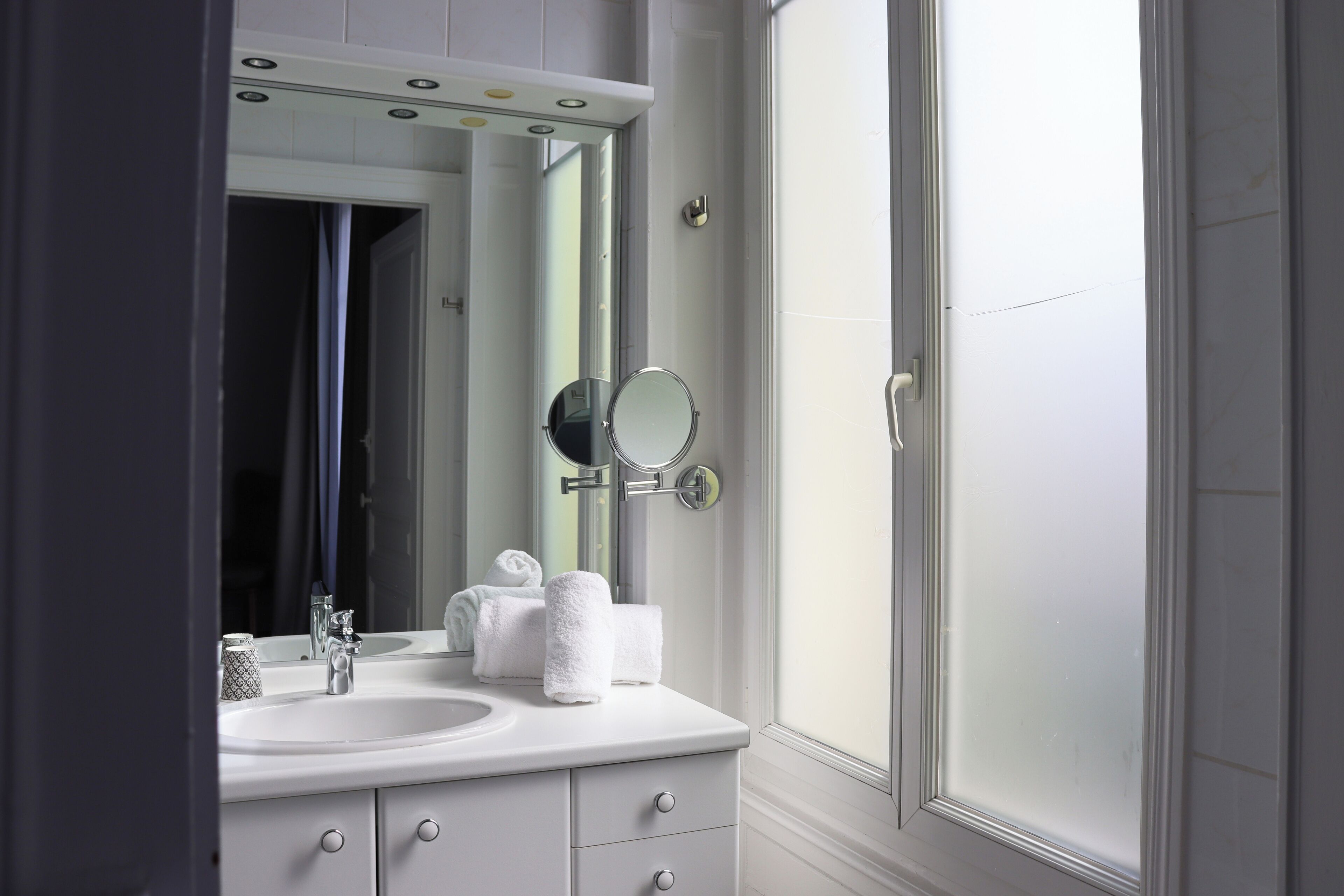 Une salle de bain avec un lavabo blanc, deux miroirs et un porte-serviettes.