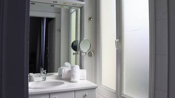 Une salle de bain avec un lavabo blanc, deux miroirs et un porte-serviettes.