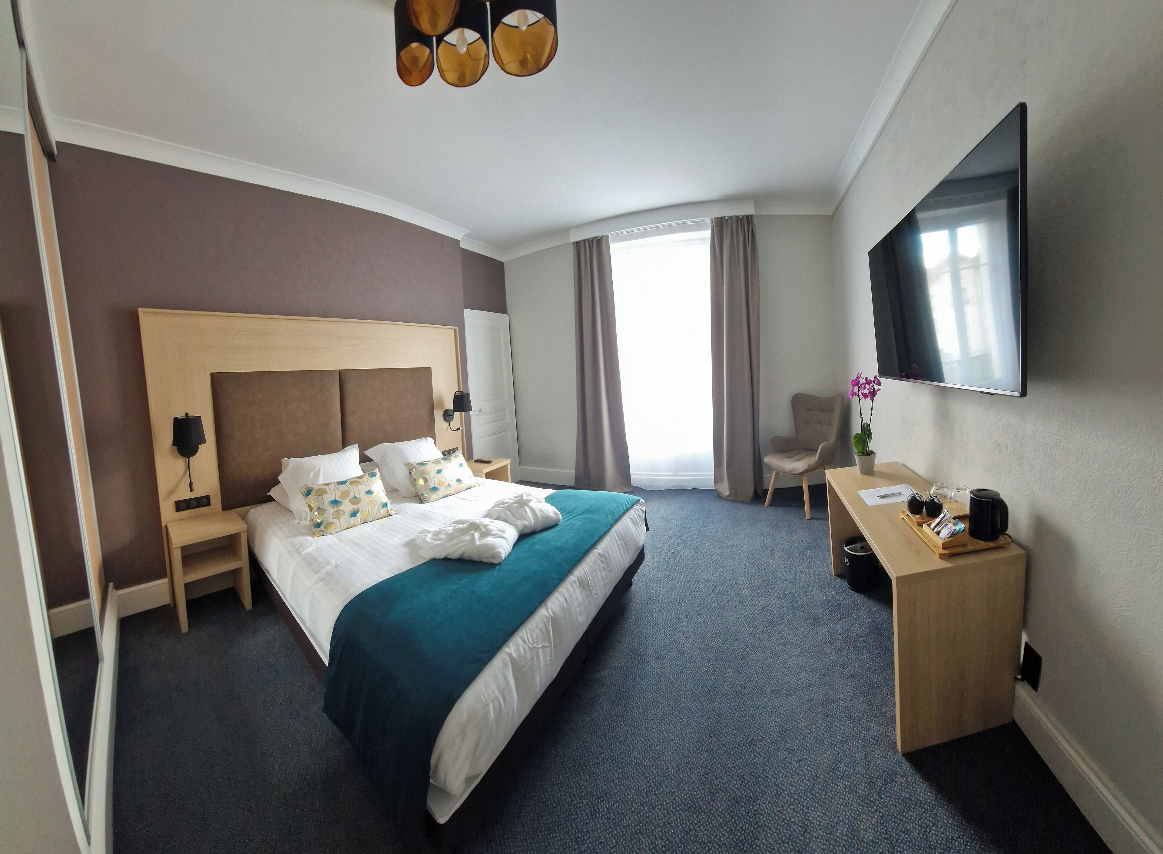 A hotel room with a large bed, a desk, a chair, a TV, and a window with curtains.