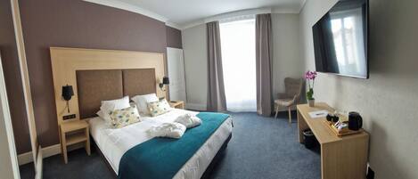 A hotel room with a large bed, a desk, a chair, a TV, and a window with curtains.