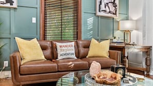 Ein braunes Ledersofa mit zwei Kissen, davon eines mit dem Aufdruck 'Wander Explore Adventure', ein runder Glastisch mit einem Stein und ein 'Nichtraucher'-Schild.