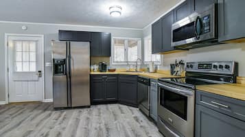 A modern kitchen with stainless steel appliances, dark cabinetry, and a wooden countertop.