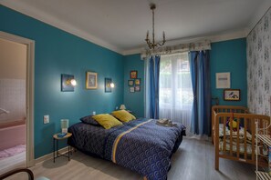 Une chambre à coucher avec un lit, un berceau, une fenêtre avec des rideaux et des lampes fixées au mur.