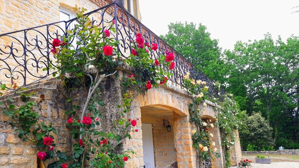 Ein Steinhaus mit einem Balkon, der mit Kletterrosen geschmückt ist.