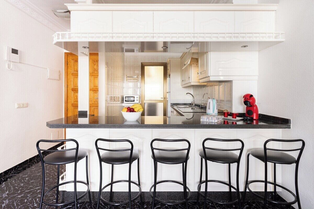 Una cocina moderna con una isla central, taburetes de bar y una tetera roja.