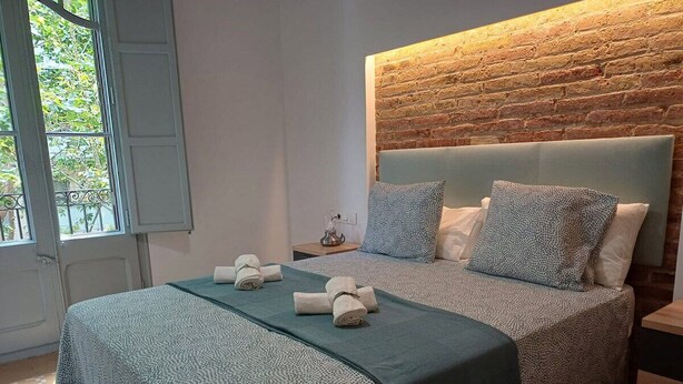 A bedroom with a brick wall, a bed with patterned bedding, and a window with a view. - LV22 Capacidad 5 personas en Poblenou, cerca playa (Barcelona)