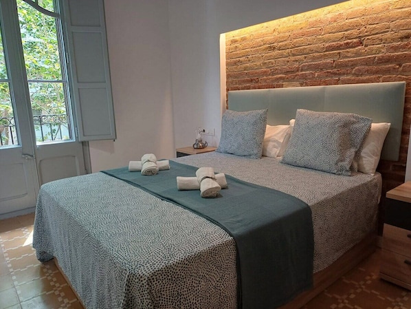 A bedroom with a brick wall, a bed with patterned bedding, and a window with a view.