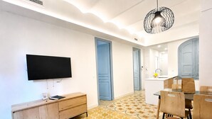 A modern hotel room with a flat-screen TV, a wooden console, a dining area with chairs, and a patterned floor. - LV22 Capacidad 5 personas en Poblenou, cerca playa (Barcelona)