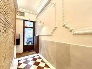 A hallway with a checkered floor, a door with a view of the outside, and decorative wall moldings.