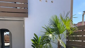 A modern outdoor seating area with two potted plants, a wooden bench, and a white wall with circular windows. - LV22 Capacidad 5 personas en Poblenou, cerca playa (Barcelona)