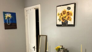 A room with a bed, a white console table with candles, a painting of sunflowers, and a door leading to another room. - Short Walk to Churchill Downs! (Louisville)