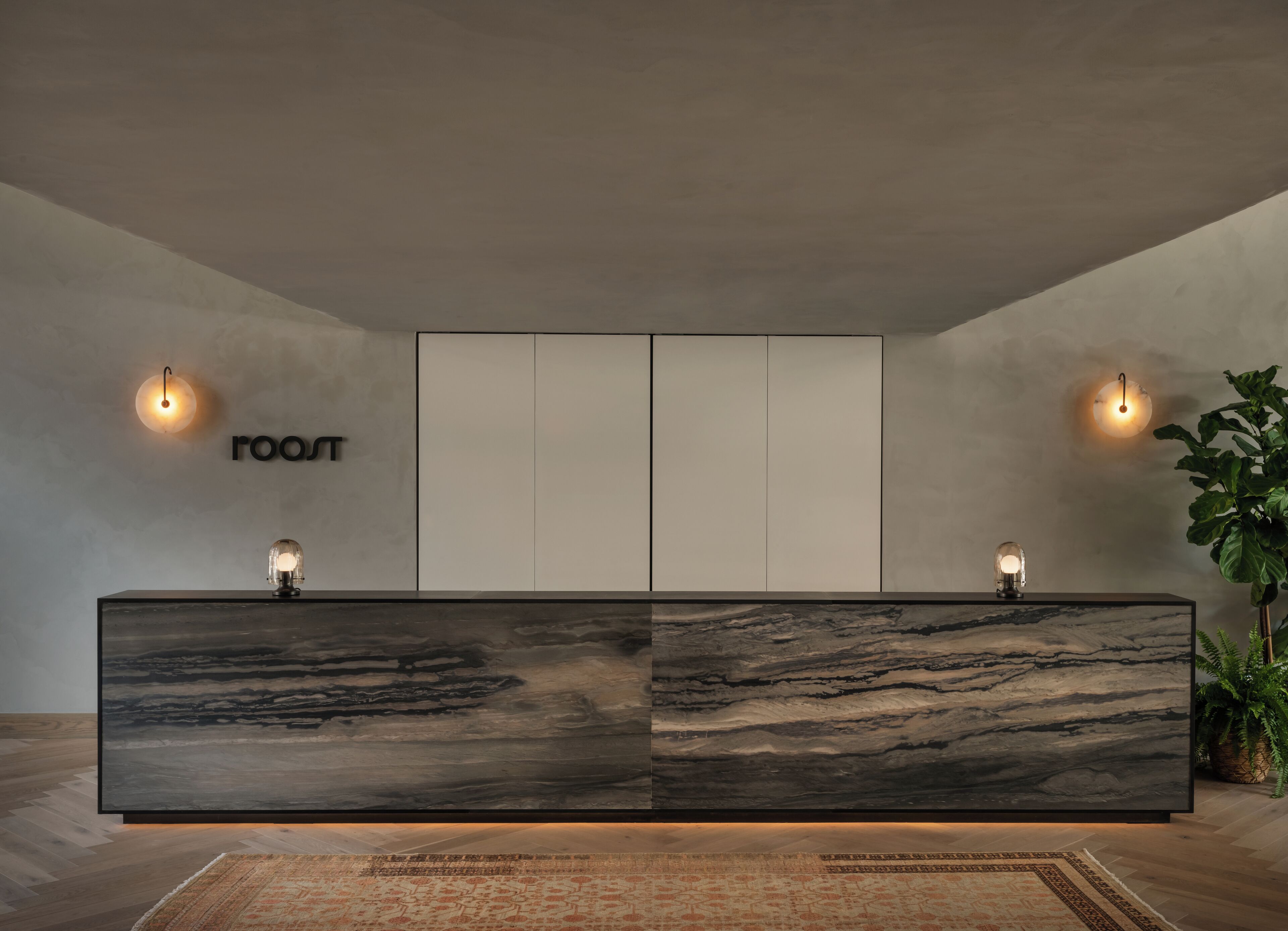 A modern reception desk with two wall-mounted light fixtures and a large, dark marble countertop.