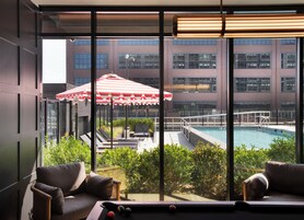 A poolside area with a view of a building, a red and white striped umbrella, and a pool.