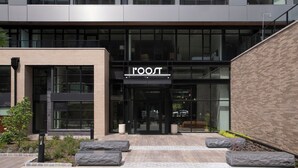 Un edificio moderno con un llamativo letrero 'ROOST', ventanas amplias y fachada de ladrillo.