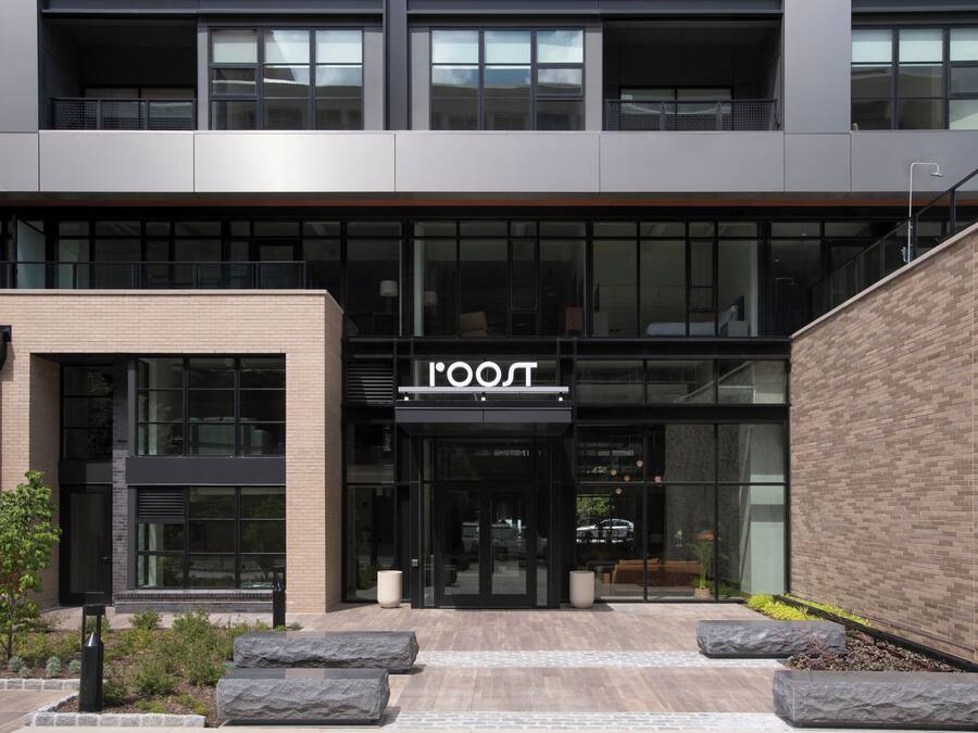Un edificio moderno con un llamativo letrero 'ROOST', ventanas amplias y fachada de ladrillo.