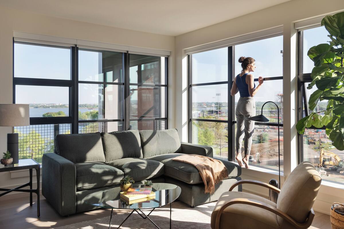 A modern living room with a large window, a gray sofa, a glass coffee table, and a view of a construction site.