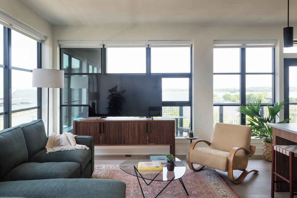 A modern living room with a large TV, comfortable seating, and large windows offering a view of the outdoors.