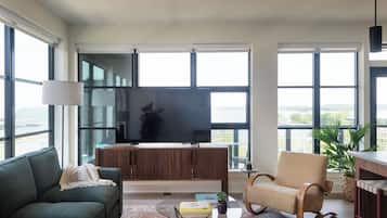 A modern living room with a large TV, comfortable seating, and large windows offering a view of the outdoors.