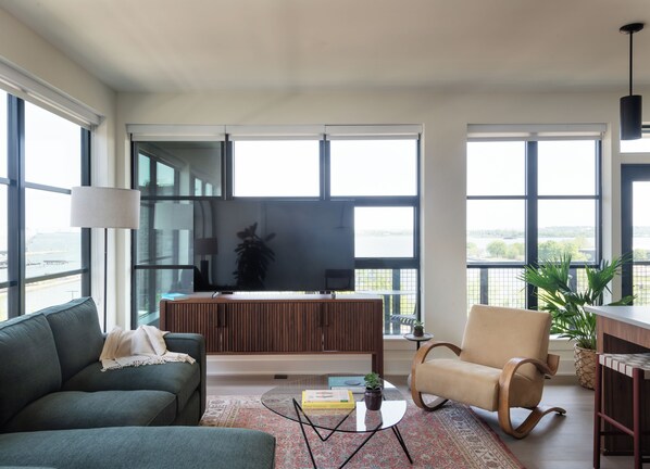 Una sala de estar moderna con un televisor grande, asientos cómodos y ventanas amplias que dan a la naturaleza.